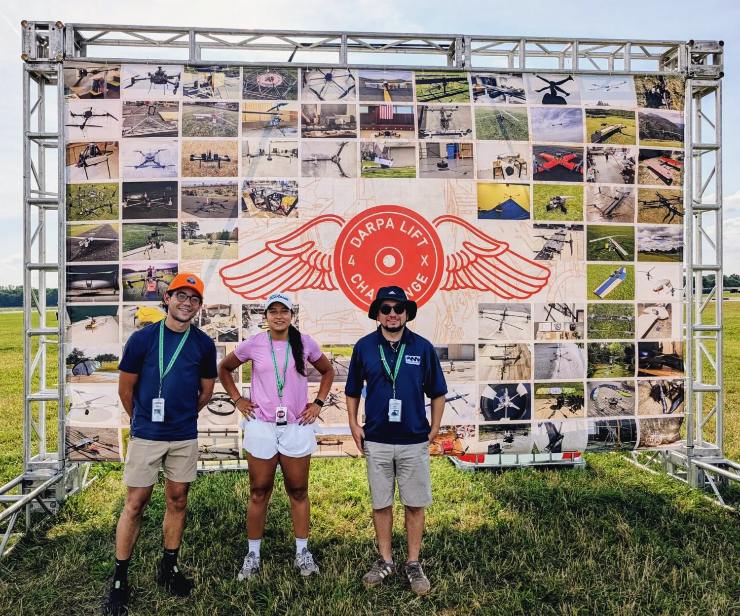 Three Max Weights team members in front of the DARPA Lift Challenge backdrop, a photo mosaic of competing aircraft.